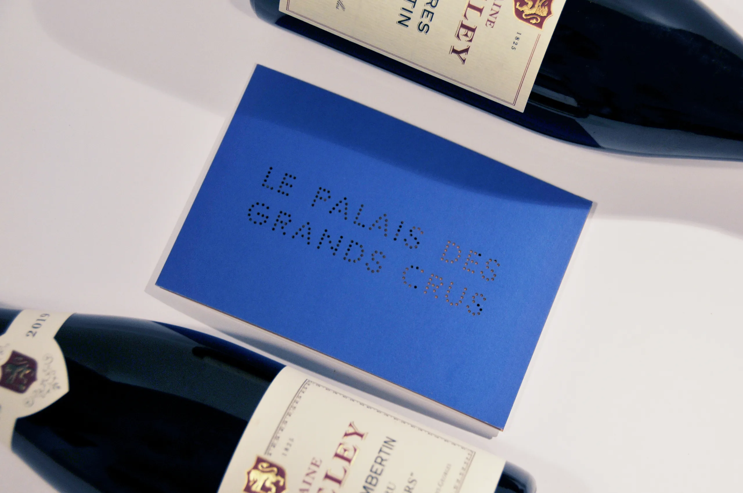 Blue Palais des Grands Crus wine programme photographed between fine-wine bottles